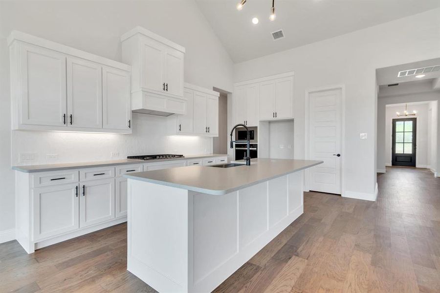 Kitchen featuring white cabinetry, custom exhaust hood, stainless steel gas stovetop, light hardwood / wood-style flooring, and a kitchen island with sink