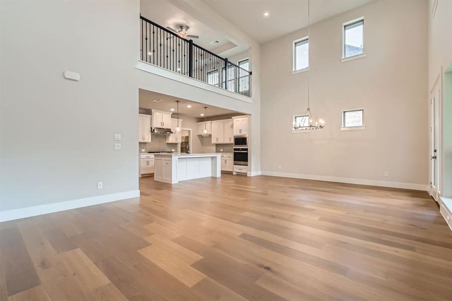 Unfurnished living room featuring a towering ceiling, a chandelier, light wood finished floors, and ceiling fan Unfurnished living room featuring a towering ceiling, a chandelier, light wood finished floors, and ceiling fan