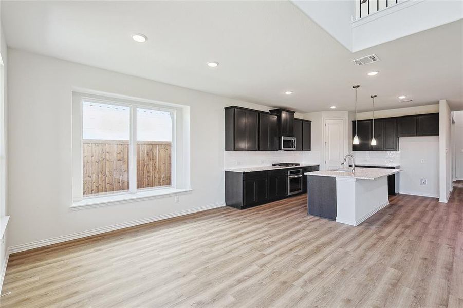 Kitchen featuring backsplash, decorative light fixtures, light wood-type flooring, stainless steel appliances, and a center island with sink