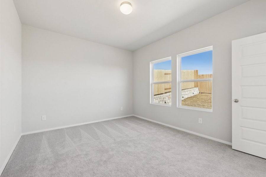 Image of a primary bedroom with light grey walls, tan carpeting, windows and white trim