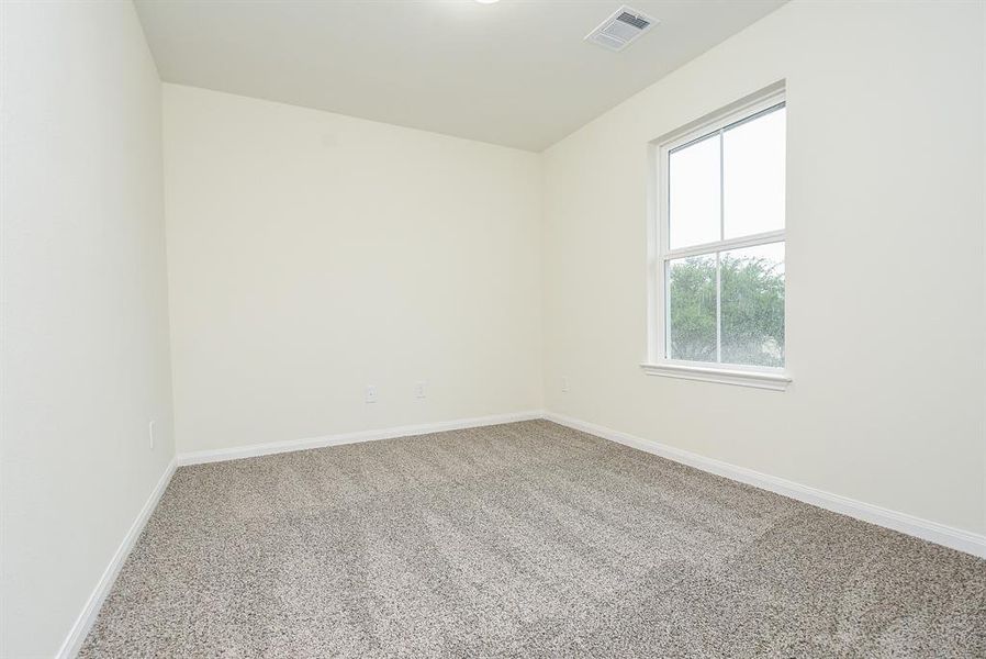 An empty room with beige walls, textured carpet, and a single window with a view of greenery outside.