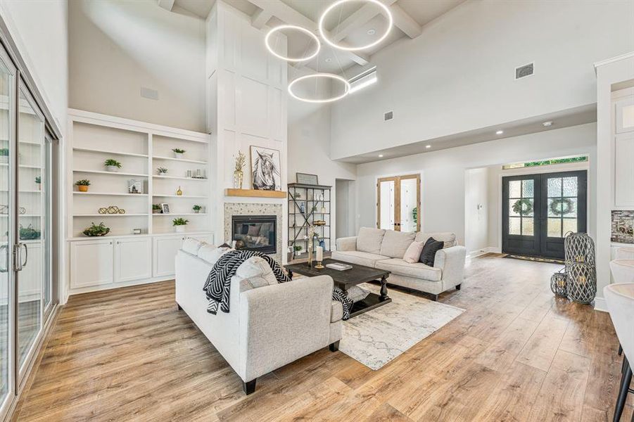 Living room with light hardwood / wood-style flooring, a fireplace, french doors, and a towering ceiling