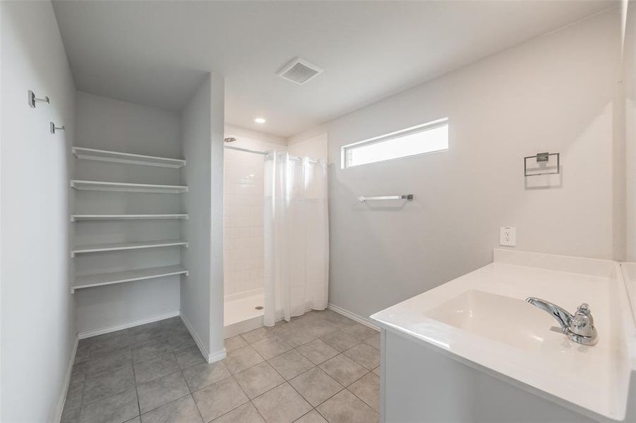 Bathroom featuring a single vanity with an integrated sink, a rectangular window, a walk-in shower with white subway tile, a shower curtain, and a built-in shelving unit