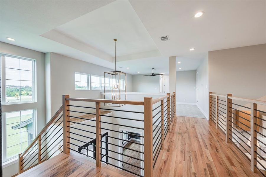 Hallway with an upstairs landing, a chandelier, recessed lighting, light wood finished floors, and a tray ceiling
