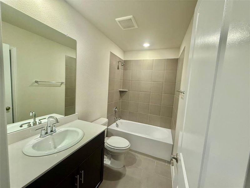 Full bathroom featuring a single vanity with a white countertop and dark wood-finish cabinetry, a toilet, and a bathtub with a tiled shower surround and an integrated shelf Full bathroom featuring a single vanity with a white countertop and dark wood-finish cabinetry, a toilet, and a bathtub with a tiled shower surround and an integrated shelf
