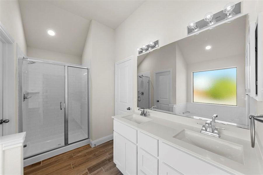 Bathroom featuring a shower stall, double vanity, wood finish floors, and recessed lighting