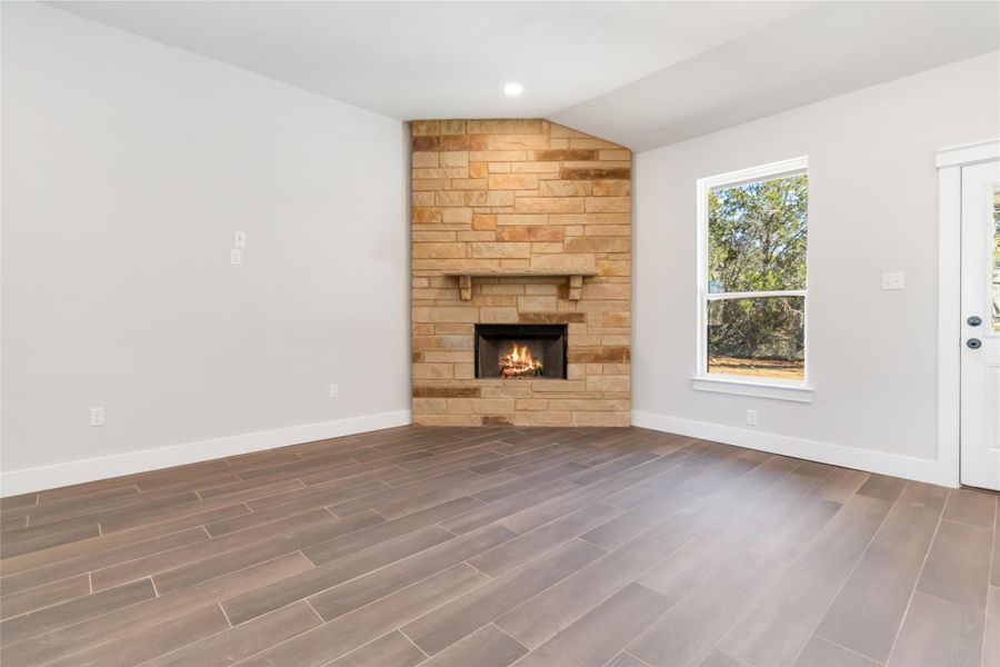 Unfurnished living room with a healthy amount of sunlight, a stone fireplace, dark hardwood / wood-style flooring, and vaulted ceiling