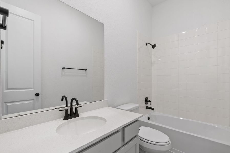 Stylish secondary bath with a shower/tub combo with a light vanity featuring gray cabinets and light countertops.