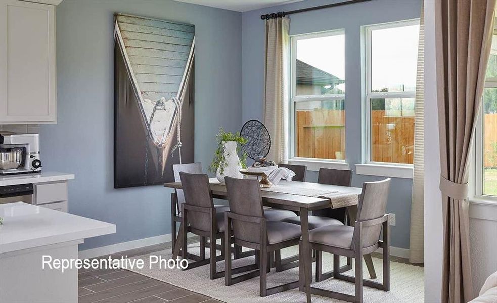 Dining area featuring a wood-finish table with upholstered chairs, multiple windows, light blue wall color, and wood-finish flooring