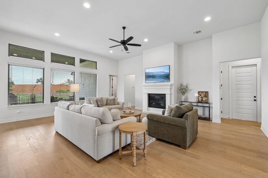 Open-concept living space featuring wood-finish flooring, a white-painted fireplace with mantel, recessed lighting, and a ceiling fan