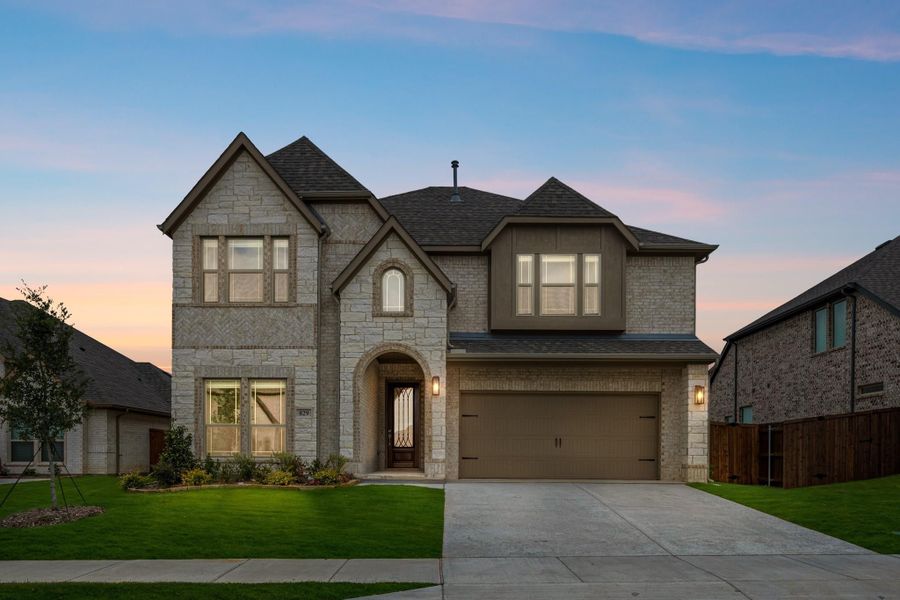 Two-story home with stone and brick exterior, arched entry, two-car garage, and green front lawn at dusk Two-story home with stone and brick exterior, arched entry, two-car garage, and green front lawn at dusk