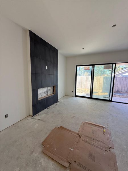 The open-concept living room features a floor-to-ceiling black tile fireplace, crafted with Amplify Matte Black 12x24 wall tile and sleek Raven grout for a striking modern statement. Expansive windows flood the room with natural light, warm white-oak flooring that extends throughout the main living spaces. The design balances warmth and sophistication - perfect for both everyday living and entertaining. The open-concept living room features a floor-to-ceiling black tile fireplace, crafted with Amplify Matte Black 12x24 wall tile and sleek Raven grout for a striking modern statement. Expansive windows flood the room with natural light, warm white-oak flooring that extends throughout the main living spaces. The design balances warmth and sophistication - perfect for both everyday living and entertaining.