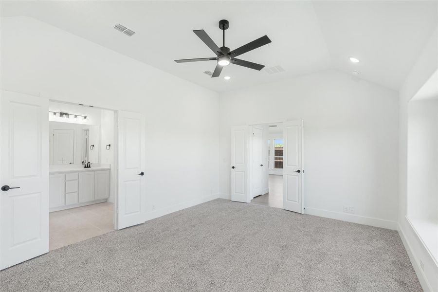 Spacious bedroom with gray carpet, black ceiling fan, and open ensuite bathroom with white vanity.