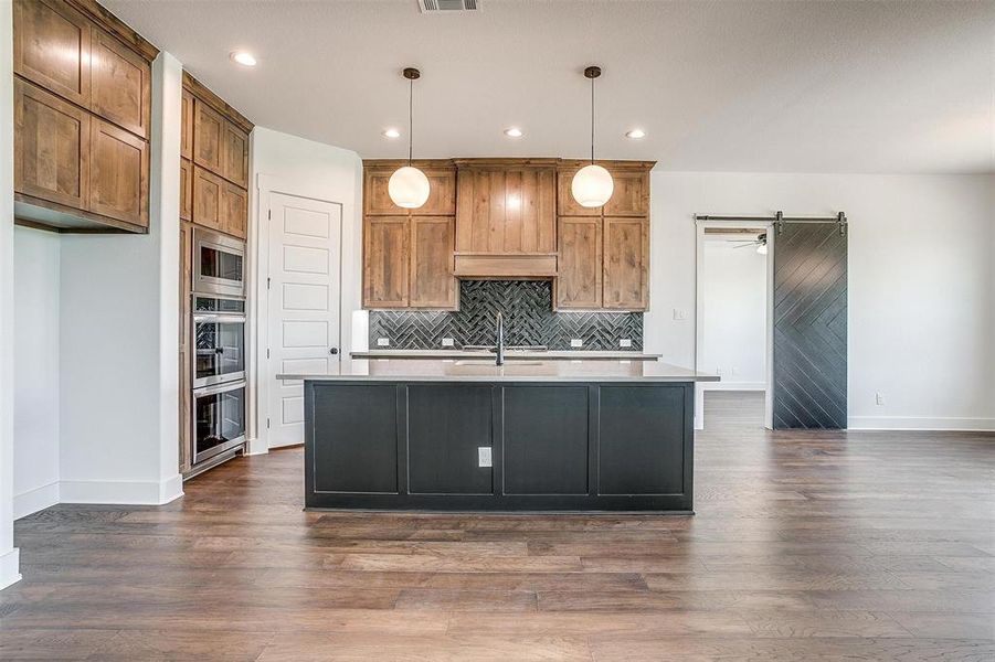 Kitchen with a center island with sink, pendant lighting, a barn door, and dark wood-type flooring