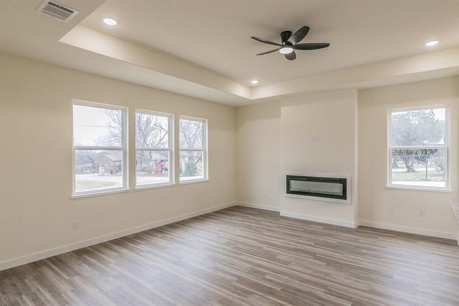 Unfurnished living room with a raised ceiling, light hardwood / wood-style floors, and ceiling fan