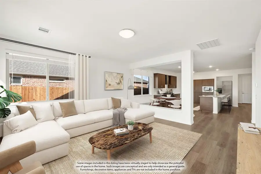 Open-concept living room with sectional sofa and hardwood floors, open to kitchen and dining area beyond