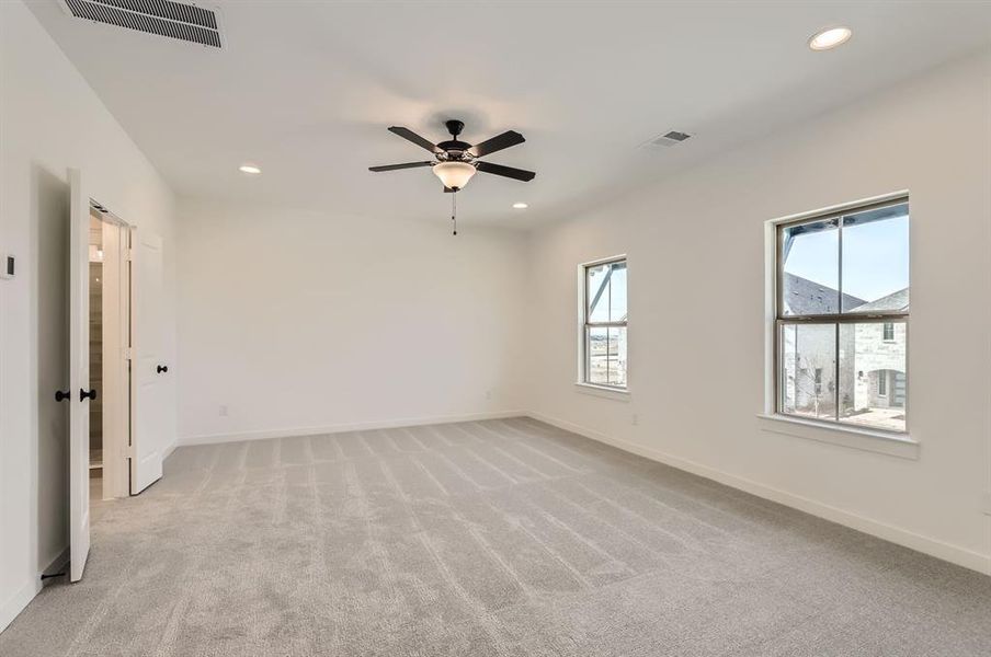 Unfurnished room featuring light carpet, ceiling fan, and a healthy amount of sunlight