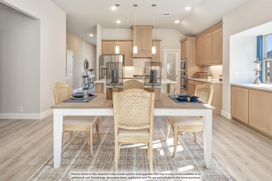 Open dining area with white table and woven chairs, flowing into kitchen with light wood cabinets and pendant lights Open dining area with white table and woven chairs, flowing into kitchen with light wood cabinets and pendant lights