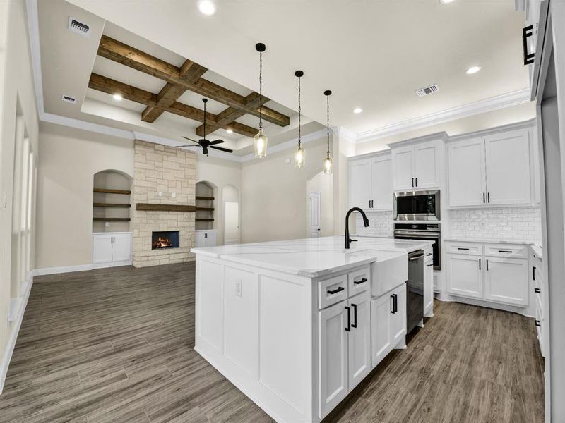 Kitchen featuring backsplash, coffered ceiling, an island with sink, beamed ceiling, and white cabinetry