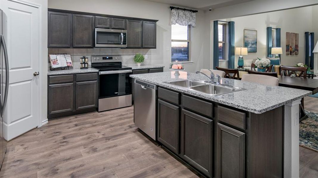 Kitchen with stainless steel appliances, backsplash, light wood-type flooring, a center island with sink, and open floor plan