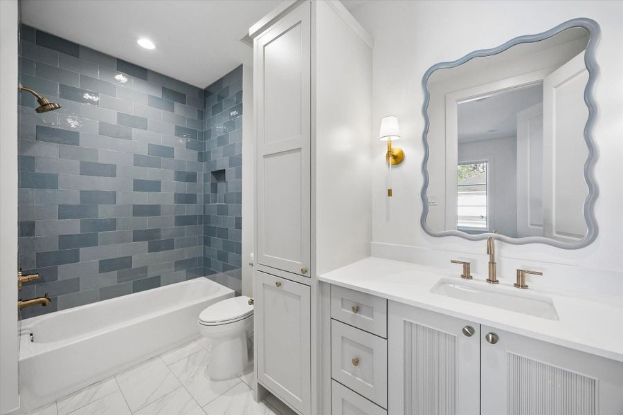 Chic secondary bath pairs a crisp white vanity with fluted cabinet detailing and warm brass fixtures for a refined finish. Glossy gray tile surround adds depth to the tub and shower, creating a polished yet playful design moment.**PREVIOUS BUILDER WORK** Chic secondary bath pairs a crisp white vanity with fluted cabinet detailing and warm brass fixtures for a refined finish. Glossy gray tile surround adds depth to the tub and shower, creating a polished yet playful design moment.**PREVIOUS BUILDER WORK**