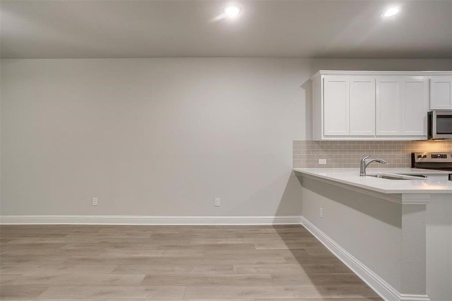 Kitchen with light wood-type flooring, light countertops, white cabinets, stainless steel appliances, and decorative backsplash Kitchen with light wood-type flooring, light countertops, white cabinets, stainless steel appliances, and decorative backsplash