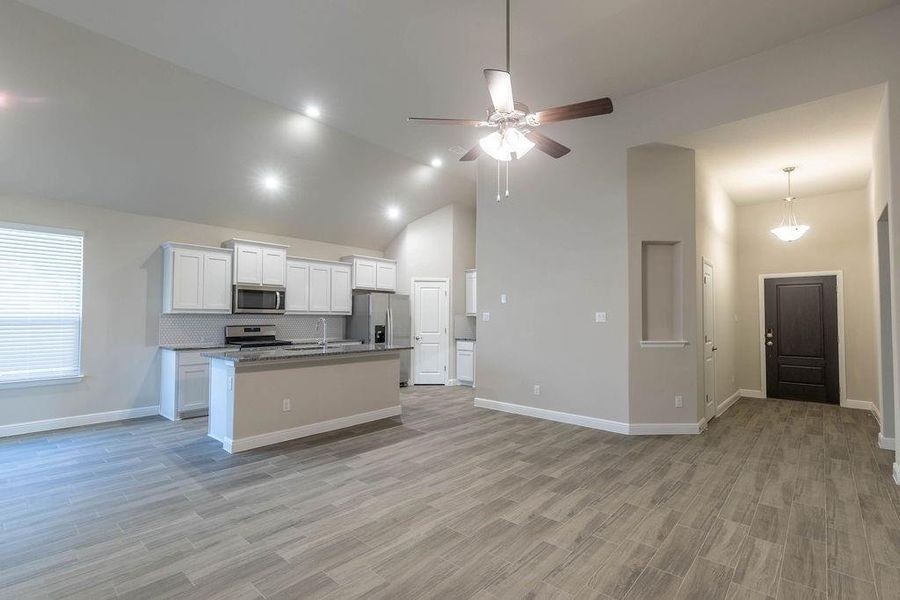 Kitchen with white cabinetry, open floor plan, light wood finished floors, a center island with sink, and stainless steel appliances Kitchen with white cabinetry, open floor plan, light wood finished floors, a center island with sink, and stainless steel appliances