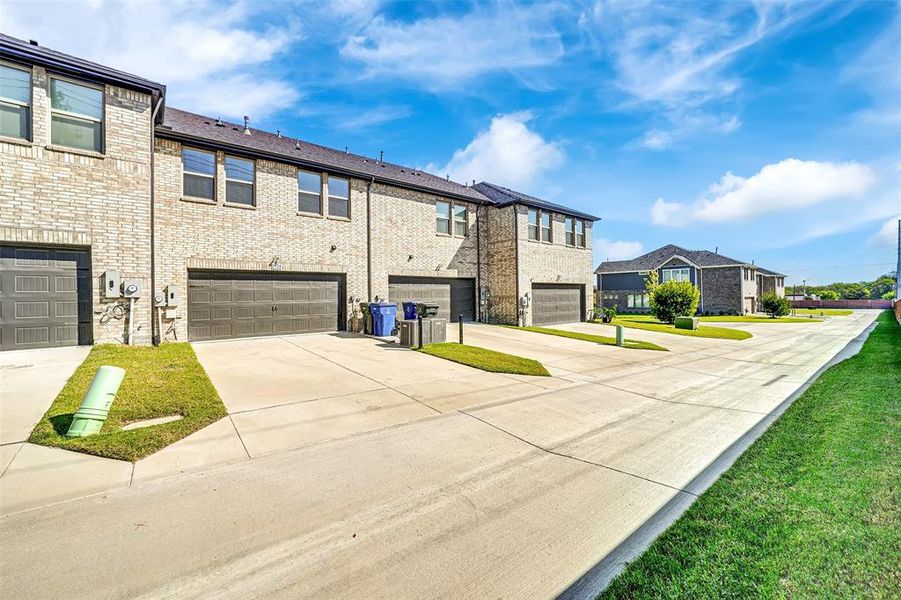 View of property exterior with concrete driveway, brick siding, a yard, a residential view, and an attached garage View of property exterior with concrete driveway, brick siding, a yard, a residential view, and an attached garage