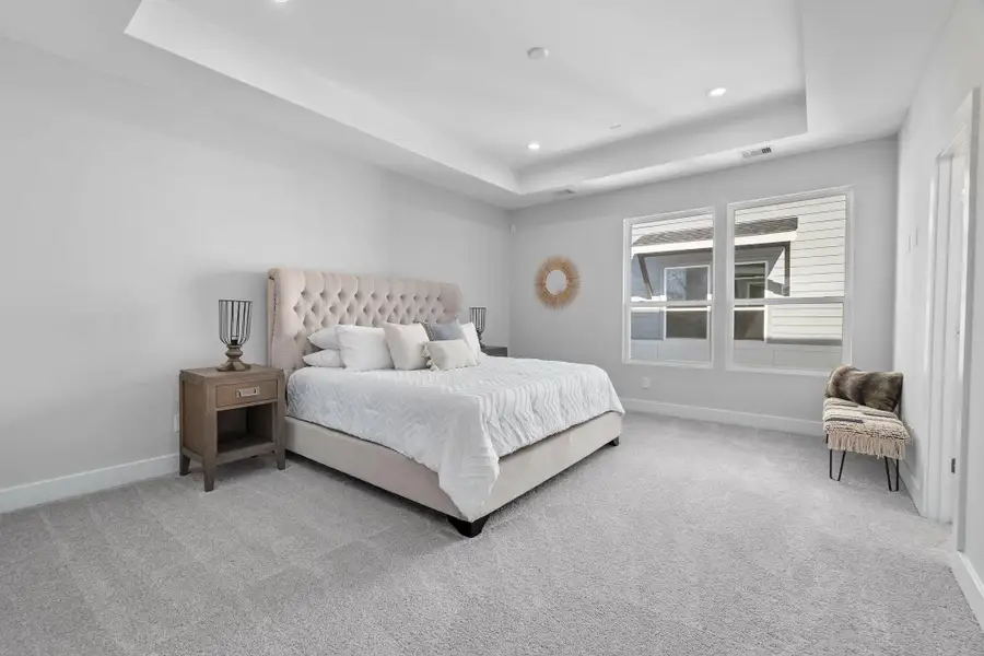 Expansive primary suite featuring tray ceilings, plush carpeting, and large windows that fill the space with natural light.