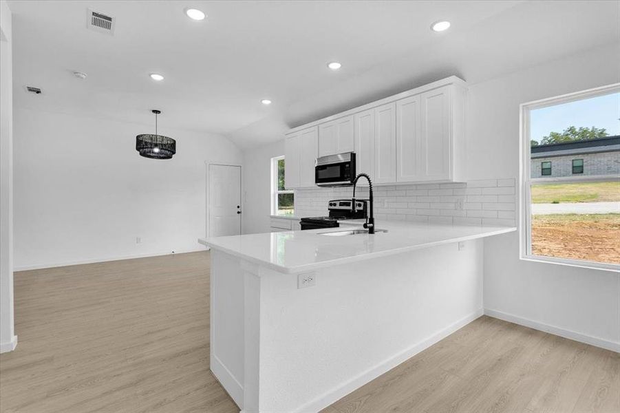 Kitchen with appliances with stainless steel finishes, light hardwood / wood-style flooring, decorative backsplash, and a wealth of natural light