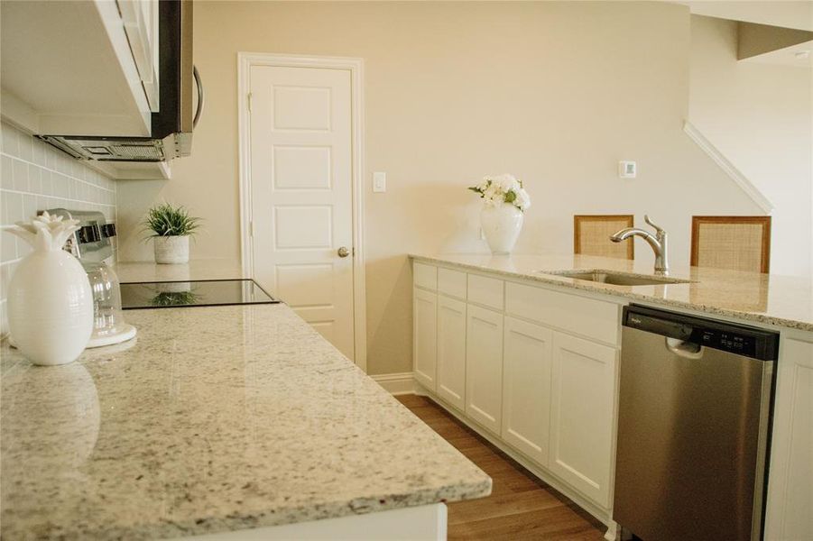 Kitchen with white cabinetry, dishwasher, sink, backsplash, and light stone countertops