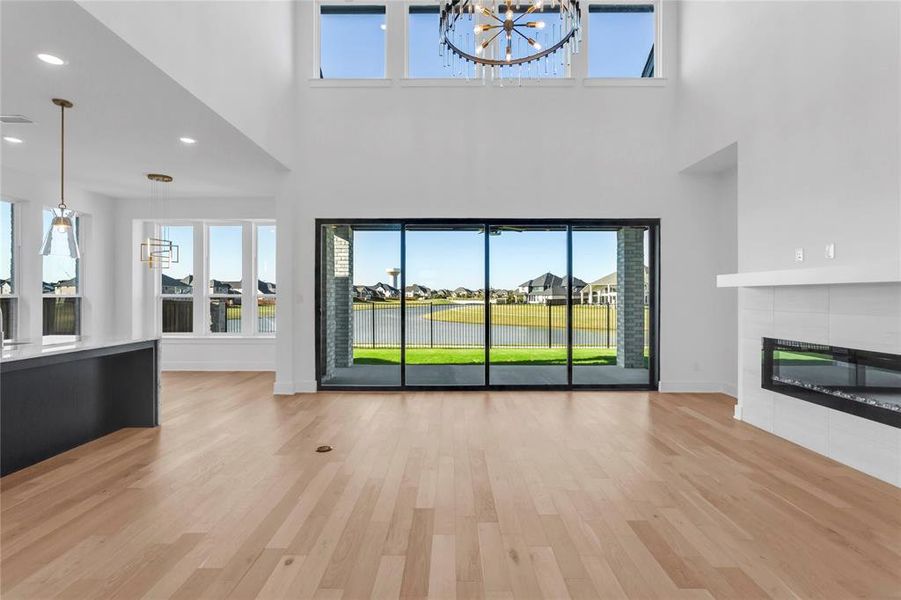 Unfurnished living room featuring light wood-style floors, a fireplace, a high ceiling, a chandelier, and recessed lighting
