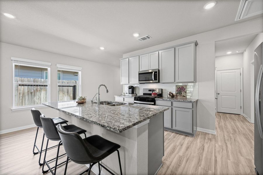 Polished granite countertops and light wood-plank flooring highlight this modern kitchen space.