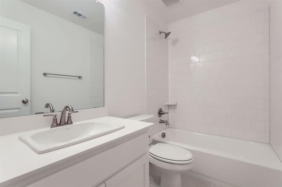 Full bathroom with tile patterned flooring, vanity, toilet, and tiled shower / bath combo