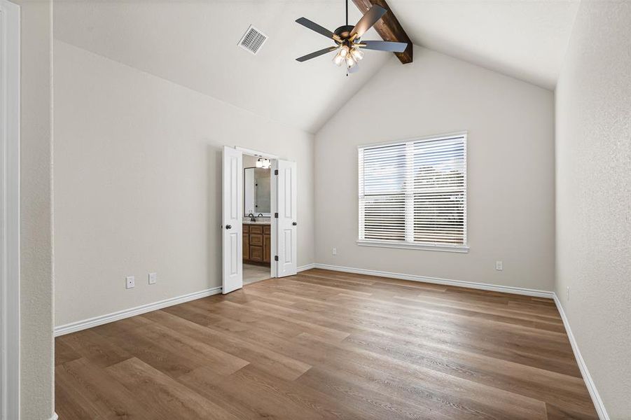 Unfurnished bedroom with beamed ceiling, light wood finished floors, a ceiling fan, high vaulted ceiling, and ensuite bathroom