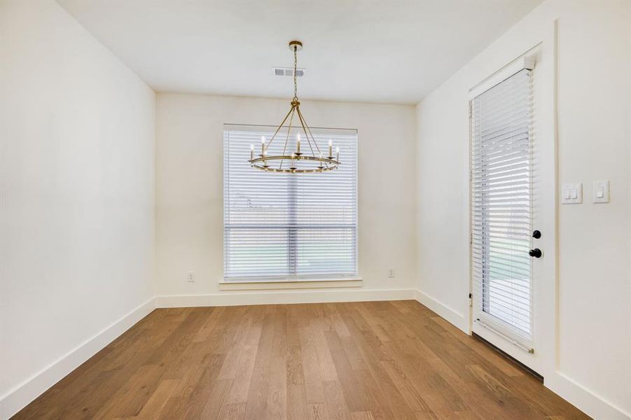 Spacious room featuring wood-finish flooring, a contemporary chandelier, a large window with blinds, and a glass-paneled exterior door