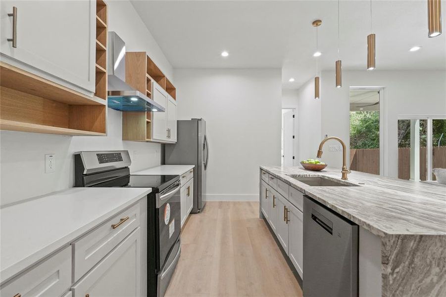 Kitchen featuring stainless steel appliances, wall chimney exhaust hood, sink, light wood-type flooring, and white cabinets