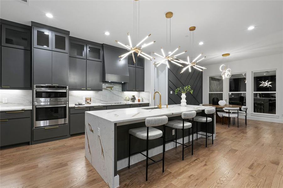 Kitchen with glass insert cabinets, stainless steel double oven, a large island with sink, pendant lighting, and a sink