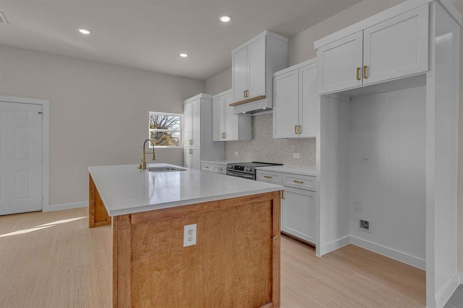 Kitchen with white cabinetry, sink, decorative backsplash, electric range, and a center island with sink