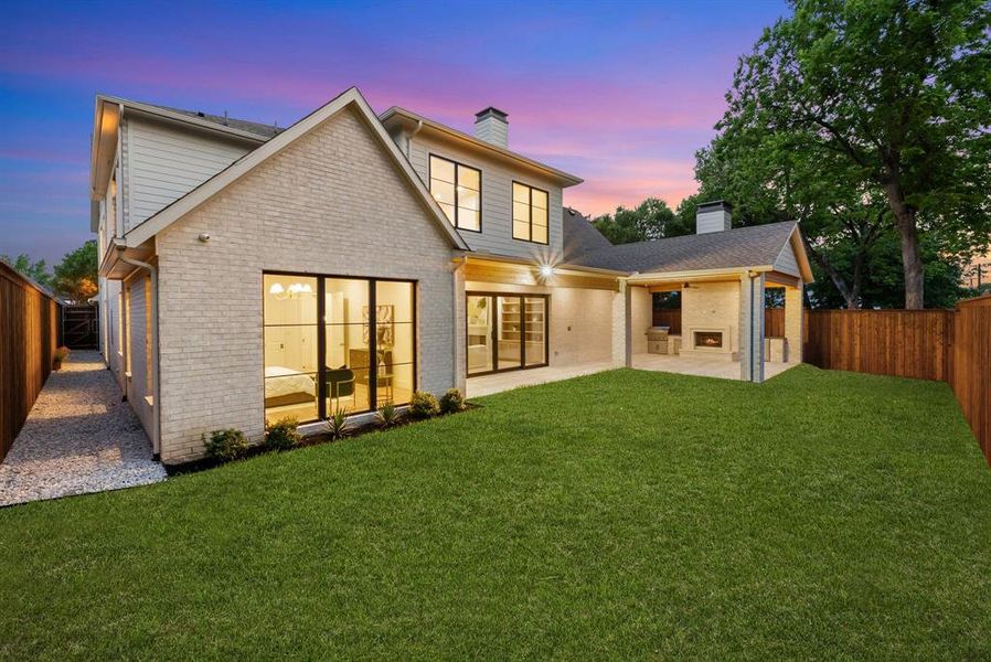 The property features an extensive lawn area, a covered patio with an outdoor fireplace, and a side walkway with gravel