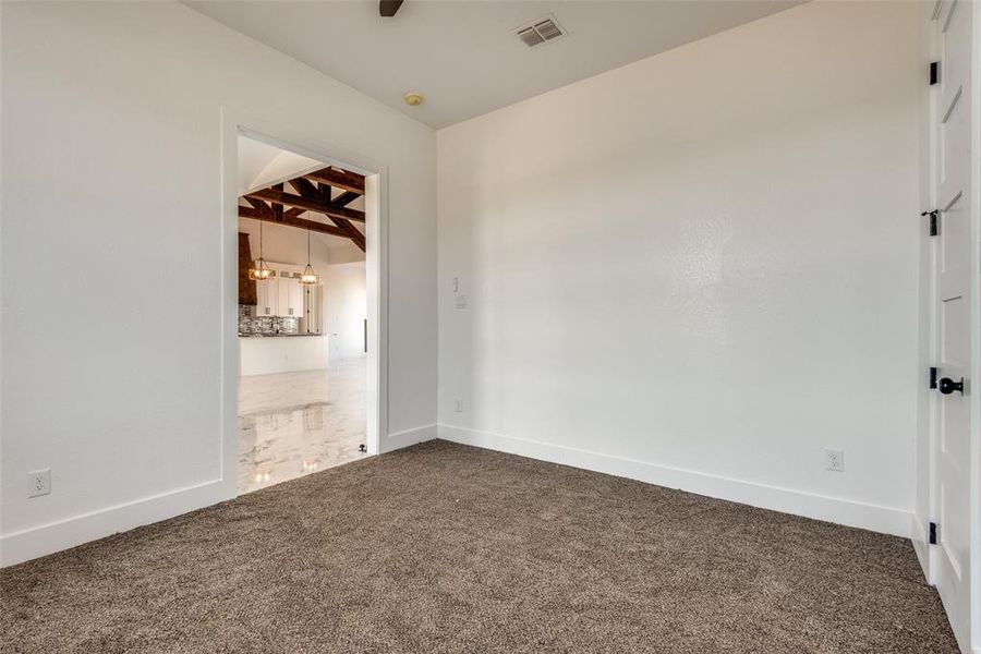 Empty room with beamed ceiling, visible vents, dark carpet, and baseboards