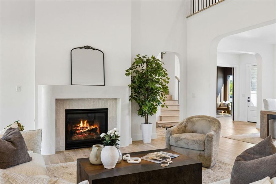 Living area with light wood-type flooring, a high ceiling, a glass covered fireplace, and arched walkways