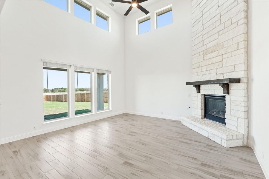 Open living room with two-story ceiling, stone fireplace, ceiling fan, and large windows overlooking backyard Open living room with two-story ceiling, stone fireplace, ceiling fan, and large windows overlooking backyard