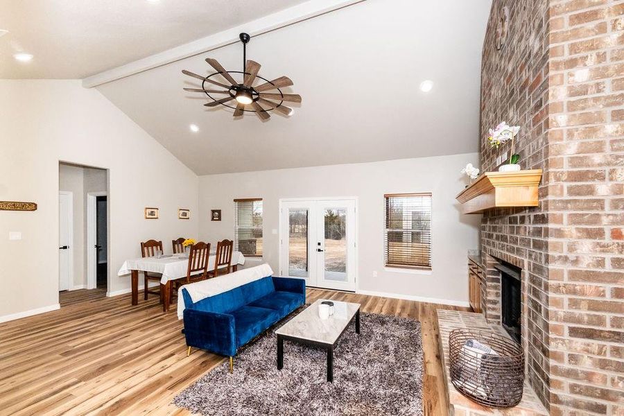 Living room featuring light hardwood / wood-style floors, vaulted ceiling with beams, a fireplace, and french doors
