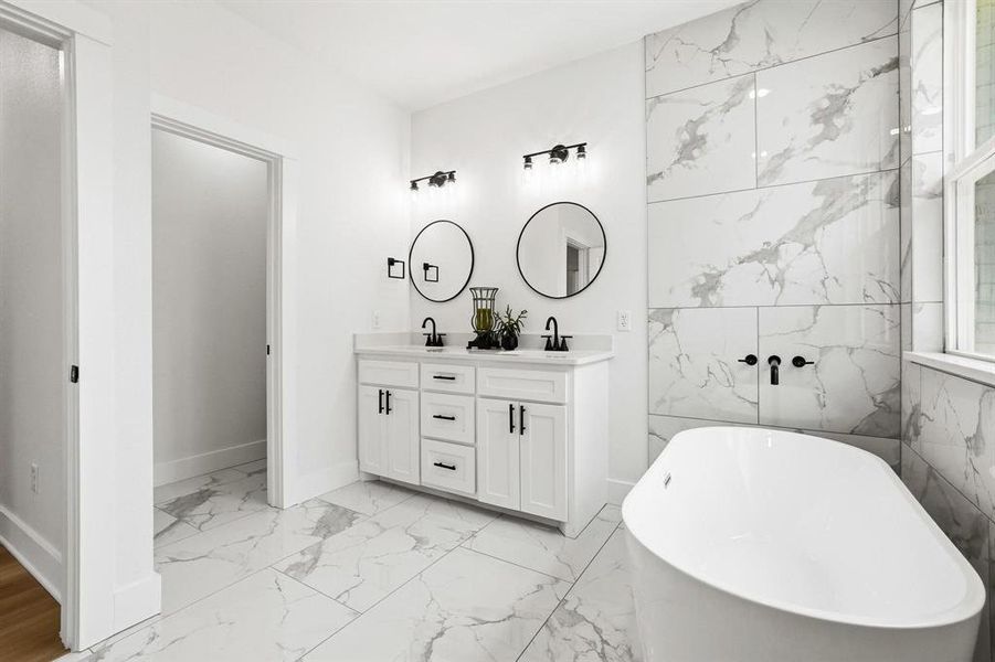 Contemporary bathroom featuring a freestanding soaking tub, white vanity with dual sinks, and large-format marble-look tile flooring and wall accents Contemporary bathroom featuring a freestanding soaking tub, white vanity with dual sinks, and large-format marble-look tile flooring and wall accents
