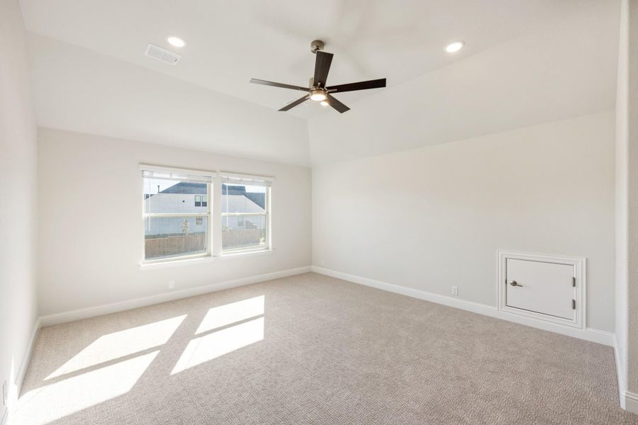Empty bedroom with vaulted ceiling, ceiling fan, carpet flooring, and a small access panel on the wall Empty bedroom with vaulted ceiling, ceiling fan, carpet flooring, and a small access panel on the wall