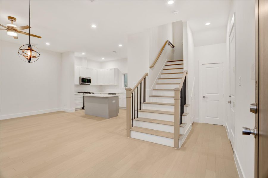 Open concept living, left to right is dining and living, kitchen is central, and to the right of stairs is a half bath then garage entry.