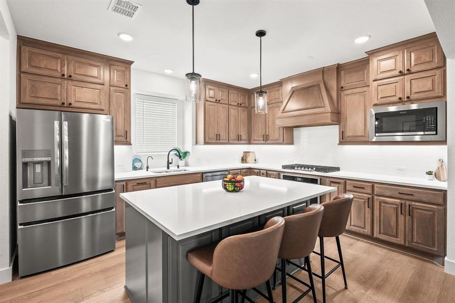 Kitchen with appliances with stainless steel finishes, light wood-style floors, a breakfast bar, decorative light fixtures, and recessed lighting Kitchen with appliances with stainless steel finishes, light wood-style floors, a breakfast bar, decorative light fixtures, and recessed lighting
