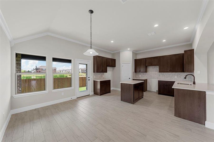 Kitchen with decorative backsplash, decorative light fixtures, dark brown cabinetry, a kitchen island, and ornamental molding