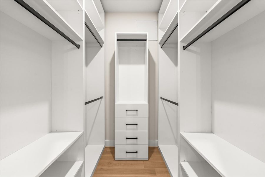 This is one of two primary walk-in closets comes fully built out with shelving, drawers, hanging space, and dedicated storage on both sides.